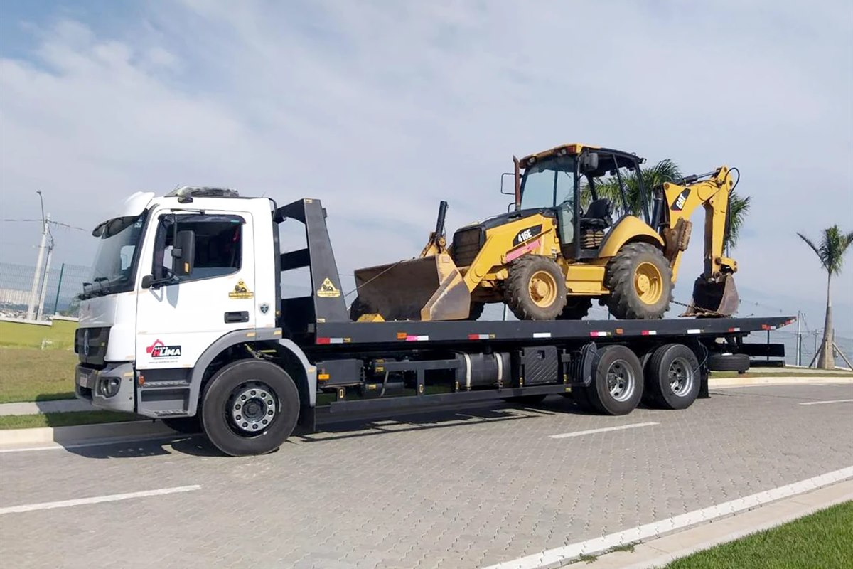 Caminhão prancha da Hloc transportando uma retroescavadeira